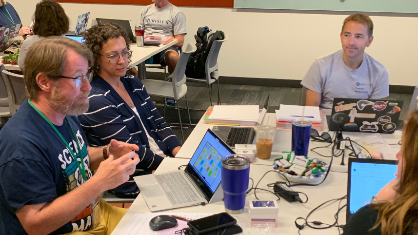 Teachers around a table engage in conversation.